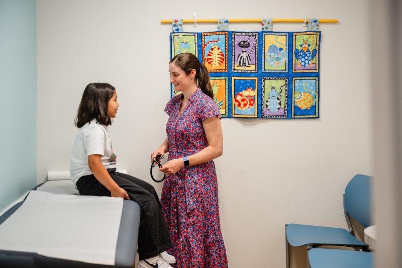 a pediatrician talking to a girl sitting on an exam table